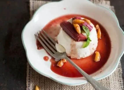Rhubarb compote with vanilla ice cream, candied pistachios, and mint garnish on white plate