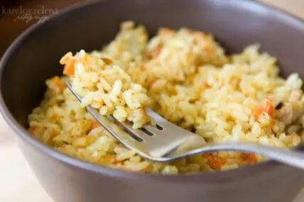 A bowl of cooked rice with vegetables and a fork
