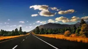 Straight highway stretching toward mountains under blue sky with golden grassland