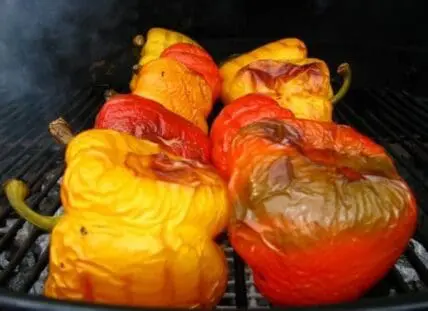 Colorful bell peppers roasting on a grill grate with charred skin.