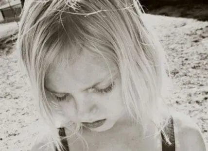 Young girl looking downward outdoors on sandy ground