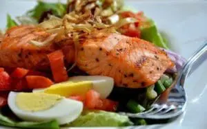 Grilled salmon fillet with hard-boiled eggs, red peppers, and green beans on a plate