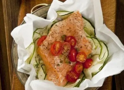 Salmon fillet with zucchini noodles and red pepper slices on parchment paper