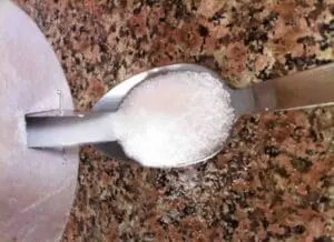 A spoon filled with white salt on a granite countertop