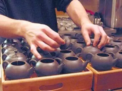Hands arranging small dark clay teapots in wooden boxes