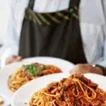 Chef in apron holding two plates of spaghetti with tomato sauce