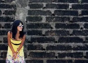 Woman in yellow dress and sunglasses leaning against brick wall