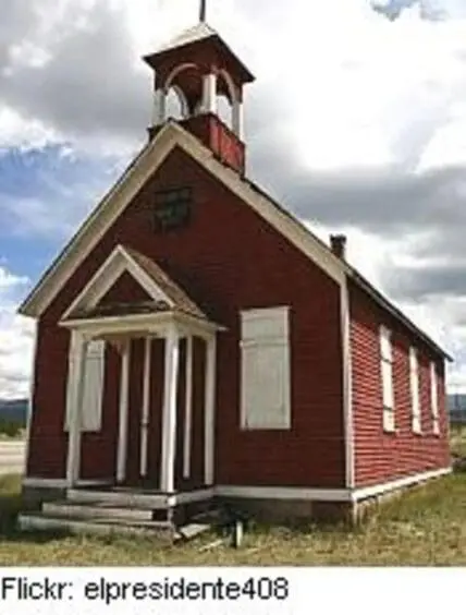Historic one-room schoolhouse with red siding and white trim under cloudy sky