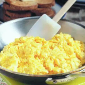 Scrambled eggs in a skillet with toast and bread in the background