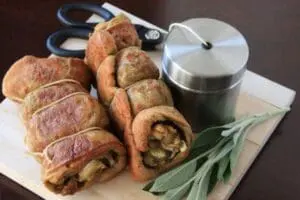 Vegetarian stuffed mushrooms and bread rolls on a wooden board with fresh sage and a butter crock