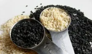 Two measuring scoops filled with black and white sesame seeds