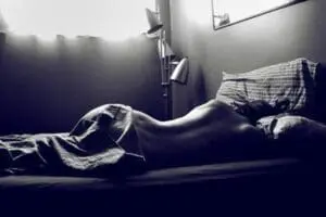 Person lying in bed with pillows and sheets in dramatic lighting