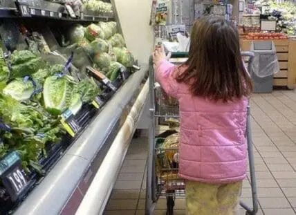 Child selecting lettuce from produce section at grocery store