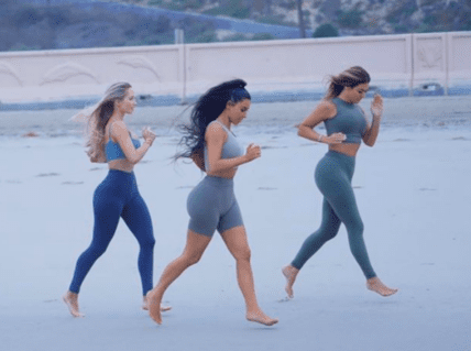 Three women running barefoot on a beach at sunrise