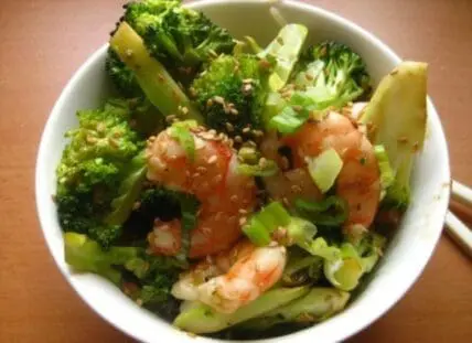 Homemade shrimp and broccoli stir-fry in white bowl with sesame seeds and green onions