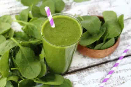 Green smoothie with spinach and fresh greens in background