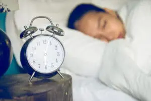 Blue alarm clock on nightstand next to sleeping child in bed