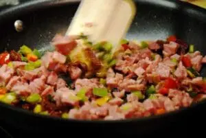 Ground meat and diced vegetables being stirred in a nonstick skillet