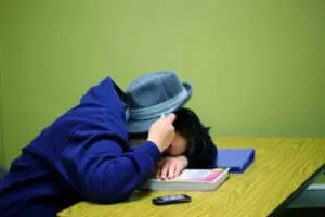 Tired person slumped over desk with hat covering face