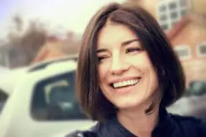 Smiling woman in dark jacket outdoors near parked cars