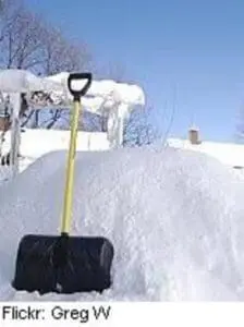Snow shovel with yellow handle stuck in snow-covered driveway