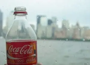 Coca-Cola bottle with condensation against rainy window overlooking city skyline