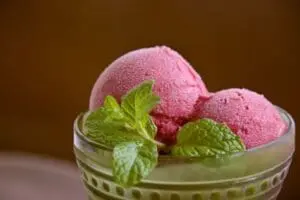 Pink sorbet scoops in a glass bowl garnished with fresh mint leaves