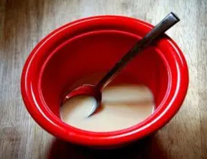 Red bowl of beige liquid with spoon on wooden surface