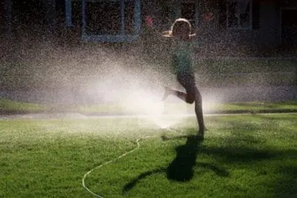 Person spraying facial mist on face during outdoor summer evening