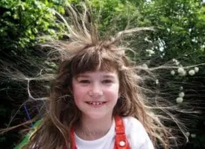 Young girl with long brown hair standing in nature with static-charged hair standing on end