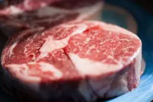 Raw red meat steak with white fat marbling on blue surface