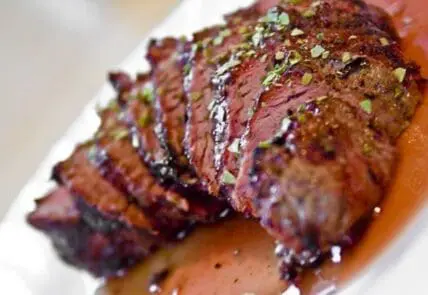 Sliced medium-rare grass-fed beef with herb crust and pan sauce