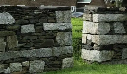 Two dry-stacked stone walls meeting at a corner in a garden setting