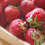 Fresh red strawberries in a white container with green stems visible