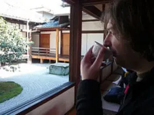 Person drinking tea while looking out window at zen garden courtyard