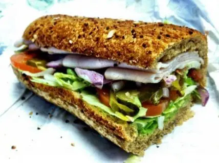 Toasted whole grain sandwich with sliced turkey, lettuce, tomato, and purple onion