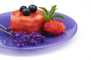 Red fruit dessert with blueberries, raspberry, and purple flowers on a purple plate