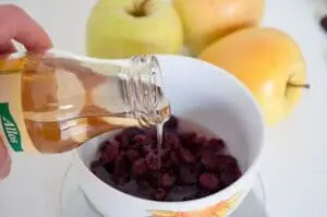 Pouring apple cider vinegar over dark berries in a white bowl