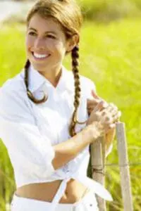 Woman in white athletic wear smiling outdoors in a sunny green field