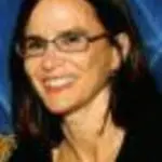Woman with dark hair and glasses smiling against blue background
