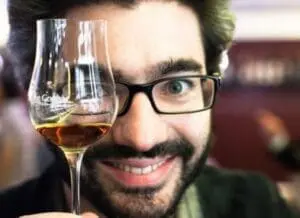 Man with beard and glasses holding a glass of amber liquid