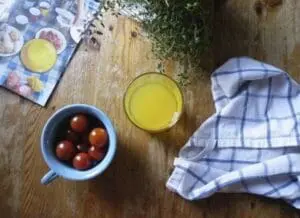Tomatoes in a bowl, olive oil, and fresh herbs arranged on a wooden table