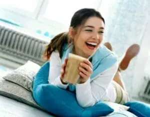Woman in blue loungewear holding a warm beverage while sitting on a bed