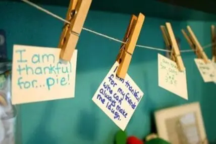 Handwritten gratitude notes clipped to a string with clothespins against a teal background.