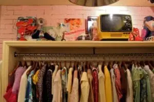 Thrifted clothing hanging on a rod with vintage items displayed on a shelf above