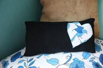 Black upcycled sweater pillow with blue bird appliqué next to blue floral bedding.