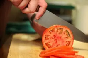 Chef's knife slicing a fresh tomato on a wooden cutting board
