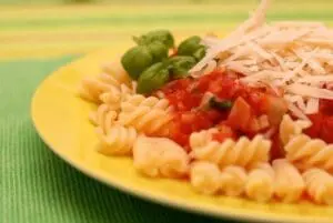 Spiral pasta with fresh tomatoes, basil, and shredded cheese on yellow plate