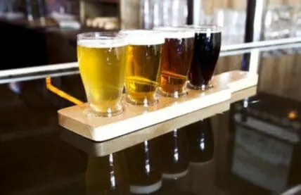 Beer flight with four glasses showing varying colors from pale yellow to dark brown
