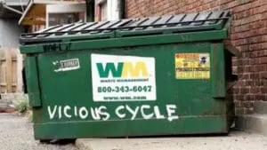 Green dumpster with "VICIOUS CYCLE" graffiti and WM Waste Management contact information